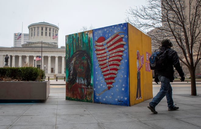 A pedestrian walks past artwork painted on plywood that was used to cover the front of the Huntington Building across the street from the Ohio Statehouse in Columbus on Tuesday. Much of the downtown area was boarded up following damage caused by protests over the summer, but the plywood window coverings have slowly gone away. Local officials asked people to stay away from Downtown through Wednesday.