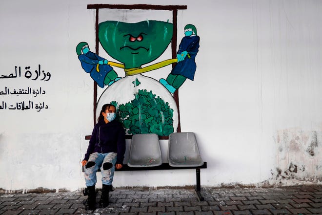 A Palestinian child sits beneath graffiti depicting medical workers fighting the COVID-19 virus outside the Health Ministry in Gaza City on Dec. 20, 2020. 