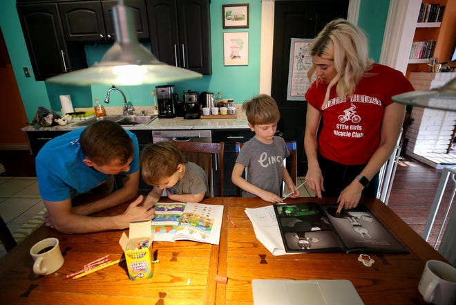 Mark Minelli, left, works with his son, Nico, 3, while Emily Minelli works with their oldest son, Tommy, 6, right, Thursday, April 2, 2020, in Cincinnati's Northside neighborhood. Emily and her husband Mark spend their weekdays switching between their full-time responsibilities as parents and workers plus his studies in graduate school.