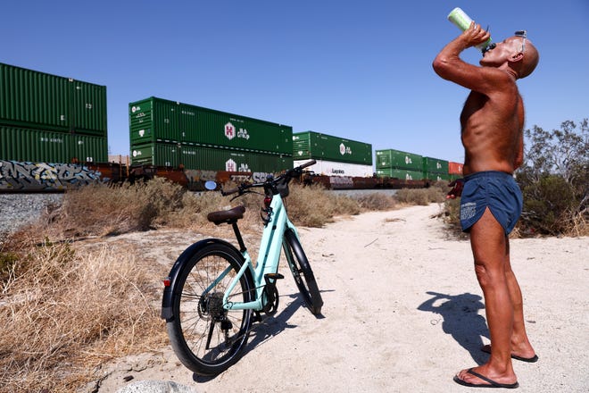 Daryl Luppino drinks from his water bottle as he takes a break during his bike ride while a train passes on July 09, 2021 near Palm Springs, California.
