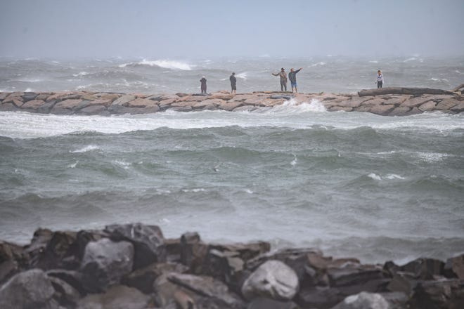 People watch the waves as they stand on a beach as Tropical Storm Henri passes, in Montauk, Long Island on August 22, 2021. - Tropical Storm Henri -- packing strong winds and heavy rain -- made landfall in Rhode Island on the east coast of the United States on Sunday, meteorologists said, with millions in New England and New York's Long Island preparing for flash flooding, violent winds and power outages.The US National Hurricane Center said in its 11:00 am (1500 GMT) advisory that Henri was 15 miles (25 kilometers) southeast of Montauk Point in New York state. (Photo by Ed JONES / AFP) (Photo by ED JONES/AFP via Getty Images) ORG XMIT: 0 ORIG FILE ID: AFP_9LH63R.jpg