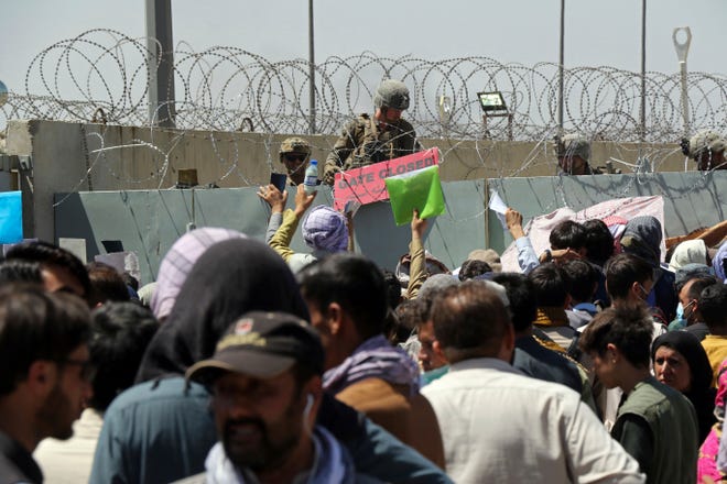 A U.S. soldier holds a sign indicating a gate is closed as hundreds of people gather some holding documents, near an evacuation control checkpoint on the perimeter of the Hamid Karzai International Airport, in Kabul, Afghanistan, Thursday, Aug. 26, 2021. Western nations warned Thursday of a possible attack on Kabul's airport, where thousands have flocked as they try to flee Taliban-controlled Afghanistan in the waning days of a massive airlift.