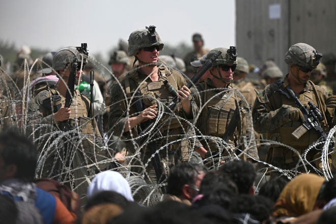 U.S. soldiers stand guard behind barbed wire as Afghans sit on a roadside near the military part of the airport in Kabul on August 20, 2021, hoping to flee from the country after the Taliban's military takeover of Afghanistan.