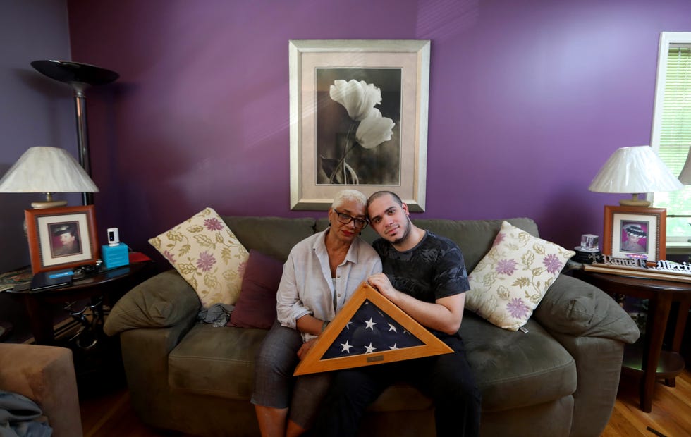 Kevin Villa, 28, and his grandmother, Ana Jager, hold the American flag that draped the coffin of his mother, Yamel Jager Merino, an EMT who was killed in the Sept. 11 attacks on the World Trade Center. A photograph of Kevin, then eight years-old, crying over the coffin of his mother received national attention. The two were photographed at Ana's home Aug. 12, 2021, where the flag, along with many photographs of her daughter, are on permanent display. 