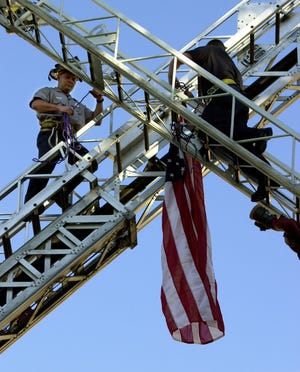 September 16, 2001: Firefighters Scott Baum, left, with the Hamilton Fire Department, and Jeff Capano, with West Chester, hang a flag between two of the departments' ladder trucks as they cross the ladders in front of the Fallen Firefighters Monument on Monument Street in Hamilton before a fire and police prayer service for the firefighters and officers who gave their lives after the Sept. 11 terrorist attacks.