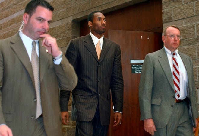 In this 2004 file photo, Kobe Bryant, center, walks out of a holding area for a lunch break from proceedings in his sexual assault case as members of his security team accompany him, in Eagle, Colo.