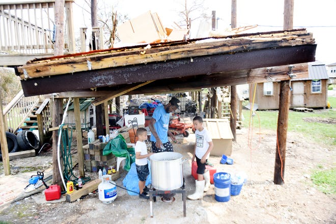 Kentrell Garner, center, uses bottled water to boil shrimp with the help of his sons, Kaviyon, left, and Mali'K, underneath what was their home Friday, Sept. 3, 2021, in Grand Caillou, Louisiana.