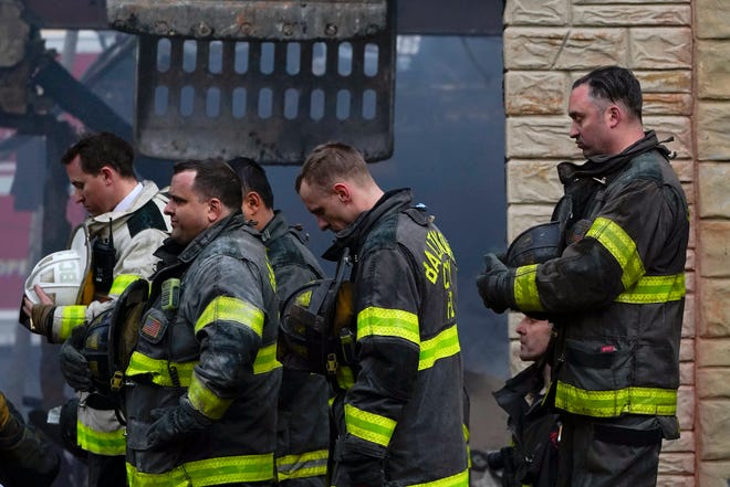 Firefighters bow their heads as a prayer is said after one of their own who died while battling a two-alarm fire in a vacant row home was pulled from the collapsed building in Baltimore.